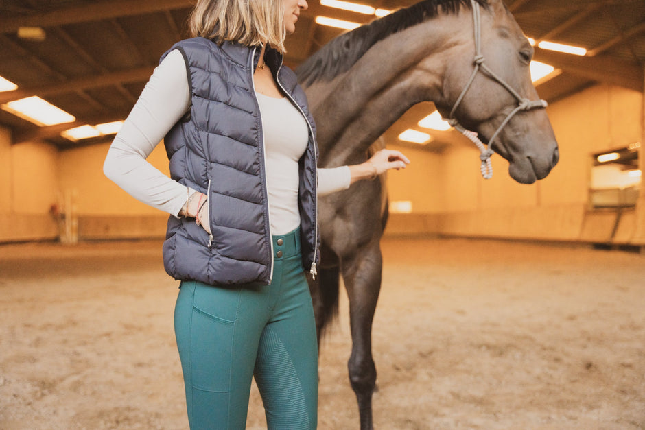 Person wearing a gilet standing next to a horse in an indoor arena