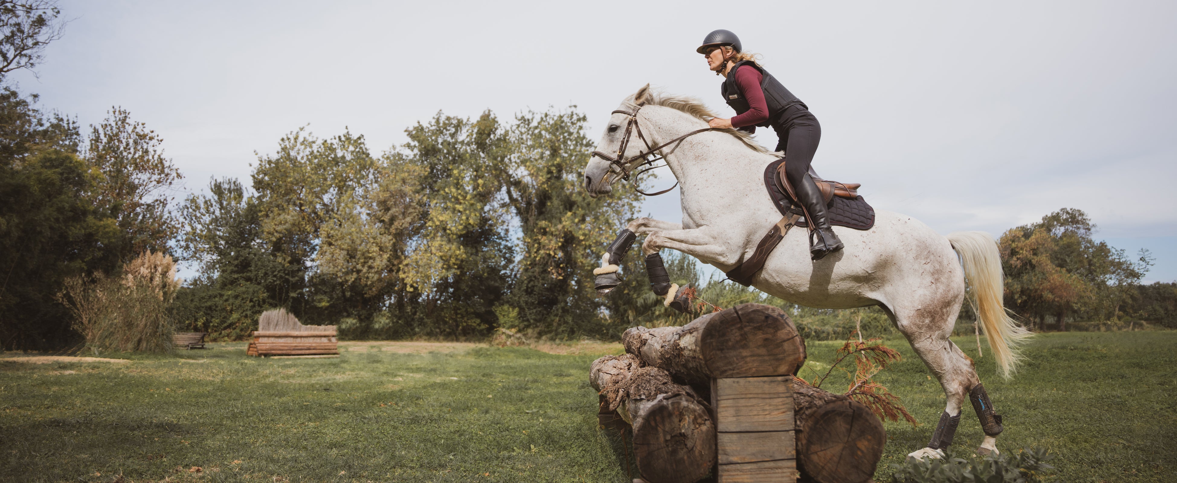 A woman riding a white horse, leaping over a wooden obstacle