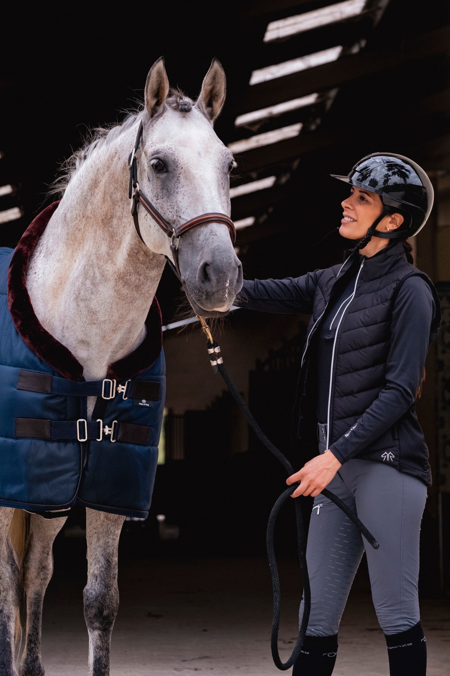 A person wearing a black jacket and helmet, standing next to a white horse